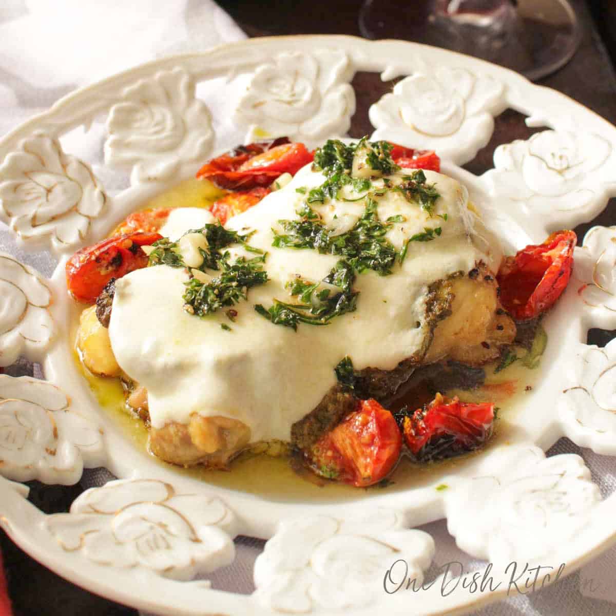 Chicken margherita on a plate with roasted cherry tomatoes next to a glass of red wine.