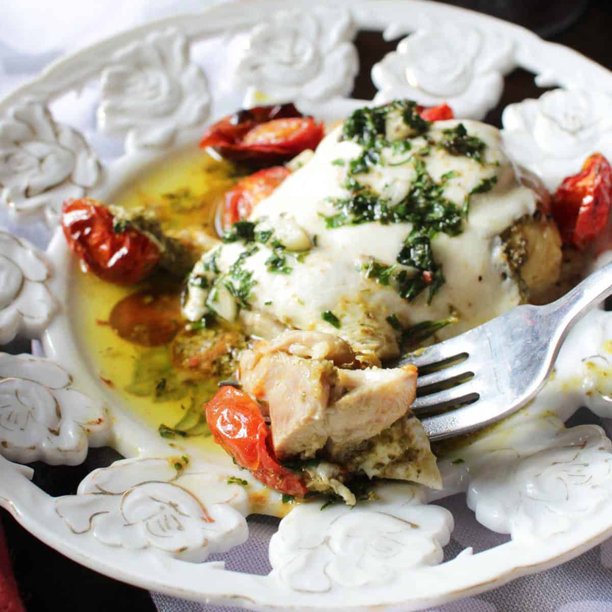 A forkful of chicken margherita from a plate with roasted cherry tomatoes. 