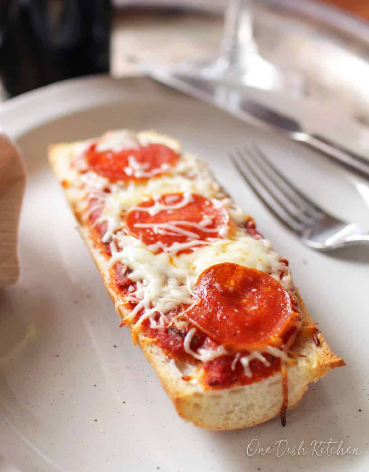 a slice of pepperoni french bread pizza on a white plate next to a fork.