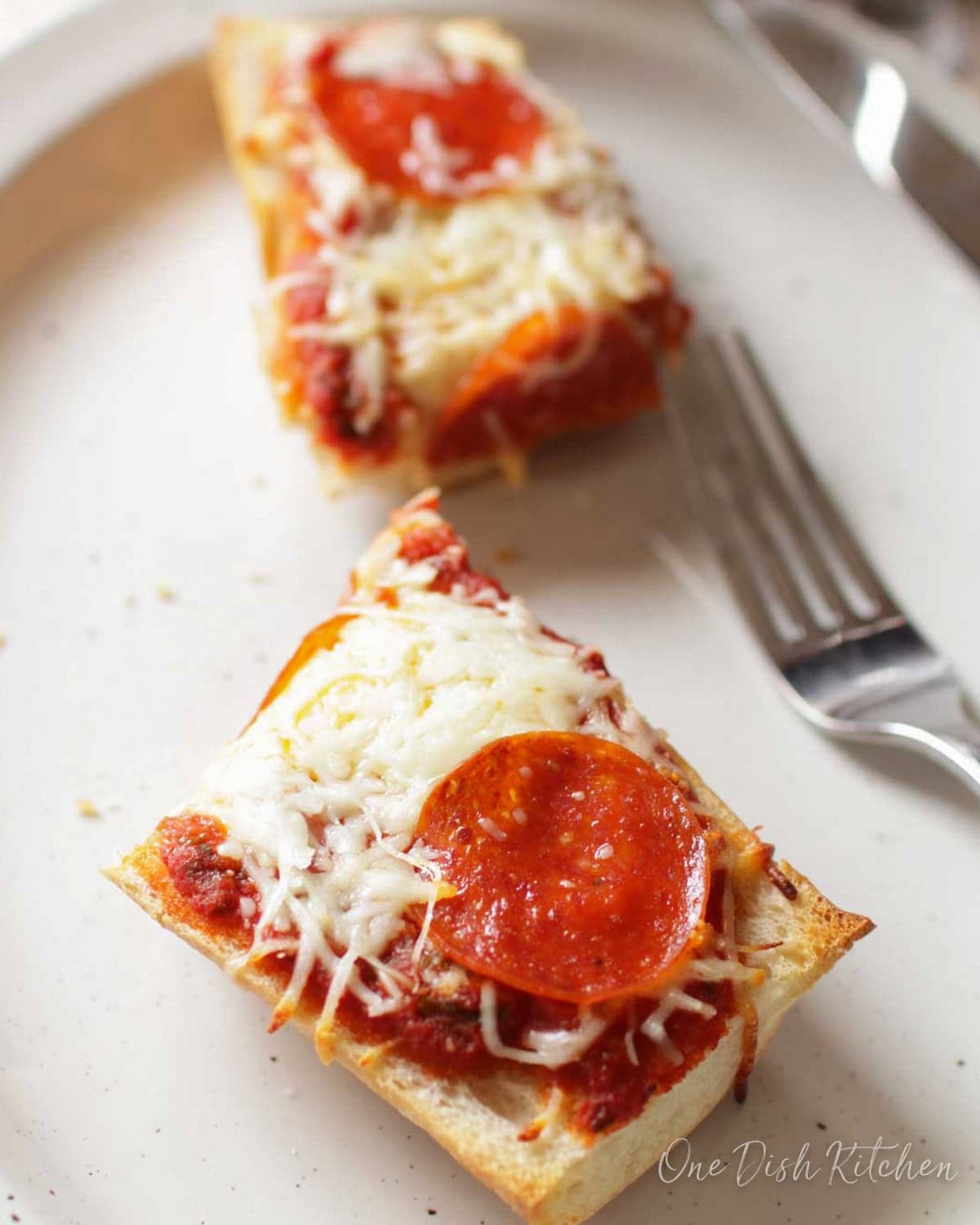 two french bread pepperoni pizza slices topped with cheese and sauce on a plate.