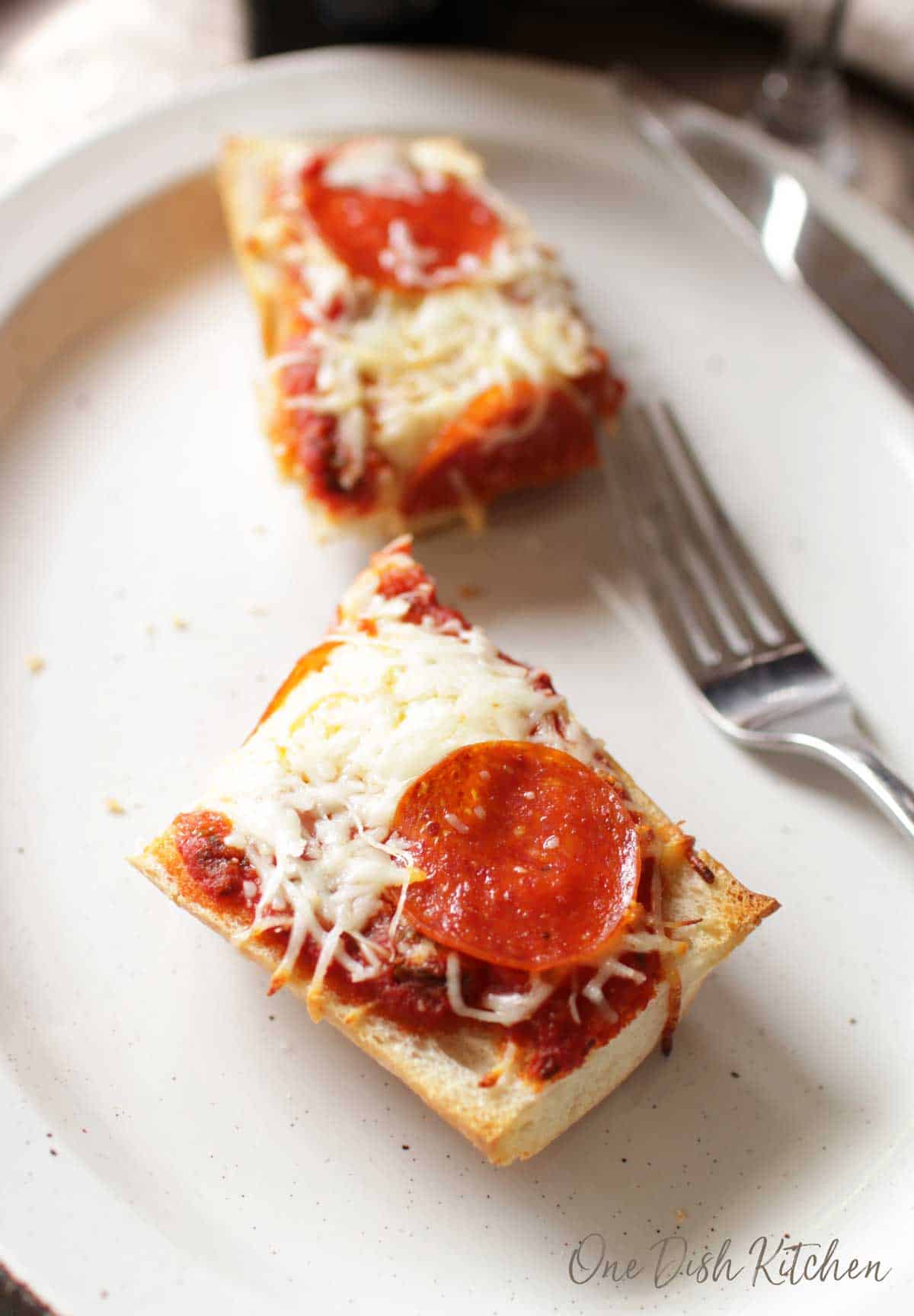French bread pizza cut in half that is topped with mozzarella cheese and pepperoni slices plated next to a fork