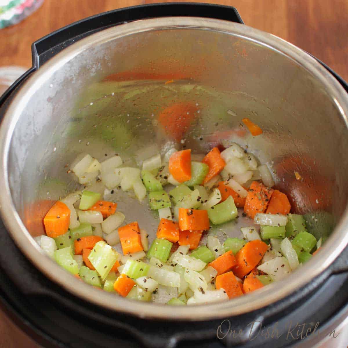 Carrots, onions, and celery cooking in an instant pot for chicken noodle soup.