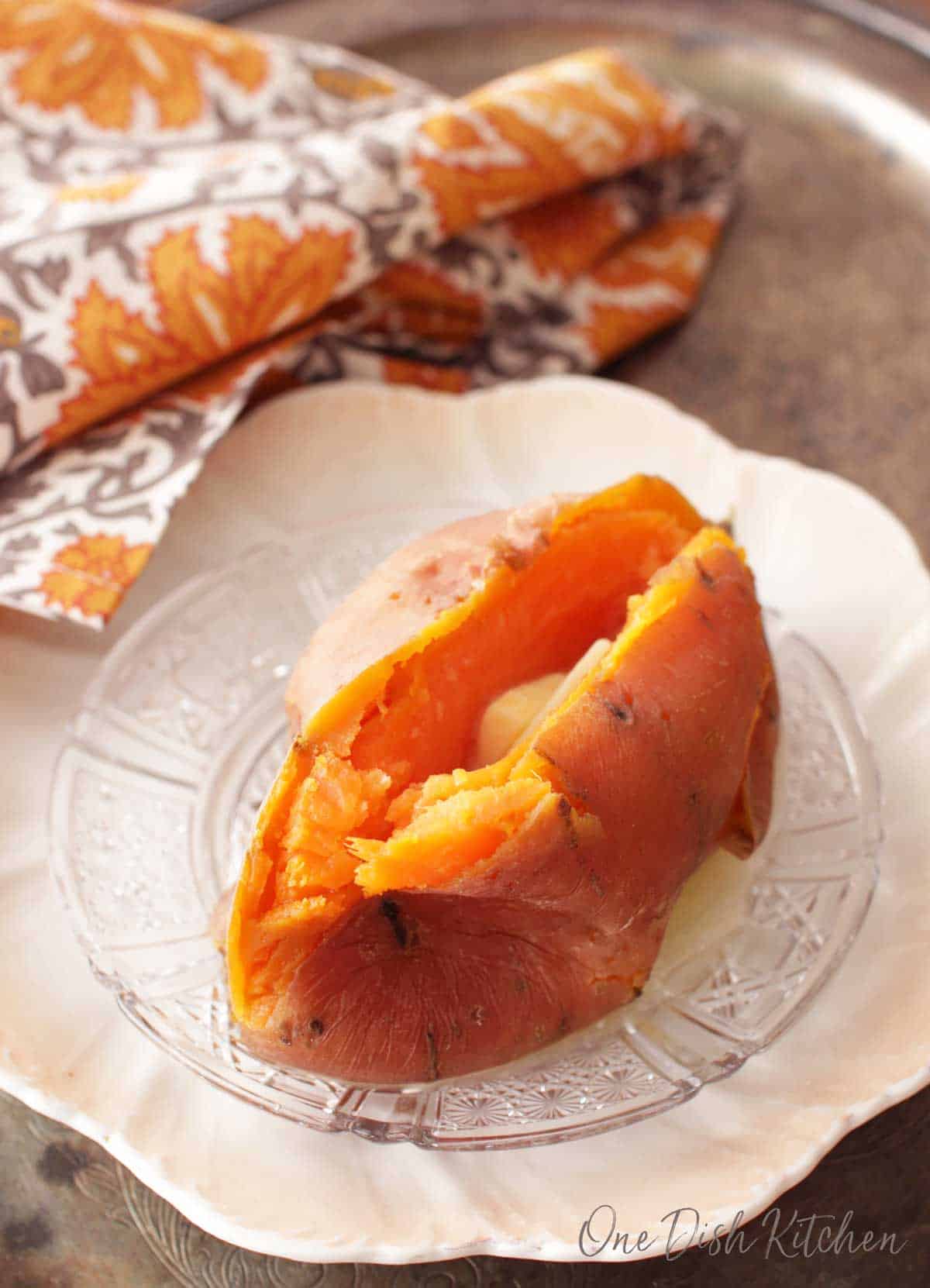 Cooked sweet potato plated on a metal tray with a grey and orange cloth napkin.
