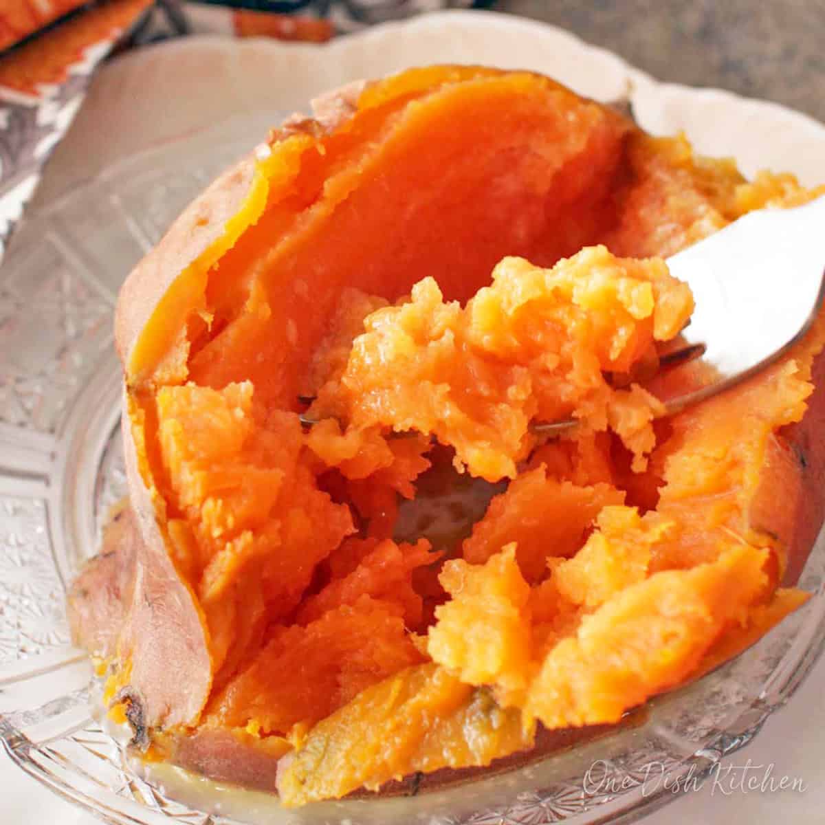 a cooked sweet potato on a plate opened up with a fork.