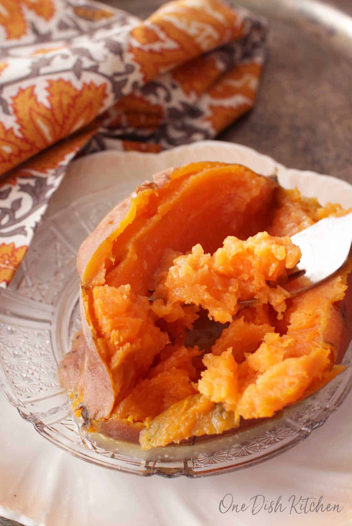 A forkful of a cooked sweet potato plated on a metal tray with a grey and orange cloth napkin.