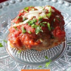 one meatball on a plate topped with tomato sauce, parmesan, and chopped parsley.