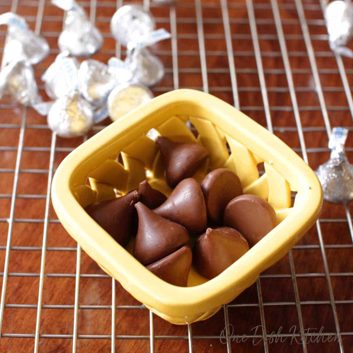 A small bowl of unwrapped hershey's kisses on a cooling rack with scattered hershey's kisses