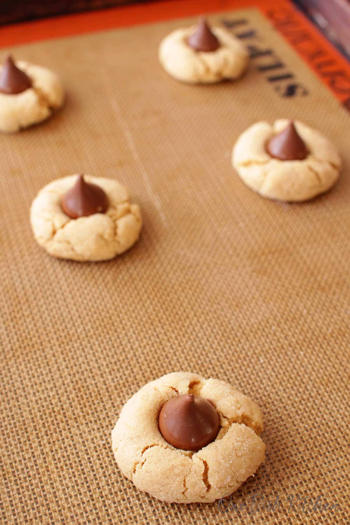 Five peanut butter kiss cookies on a baking sheet