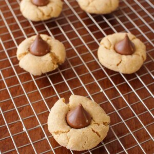 Five peanut butter kiss cookies on a cooling rack on top of a wooden table