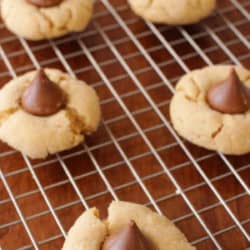 peanut butter cookies topped with a chocolate hershey's kiss on a cooling rack.