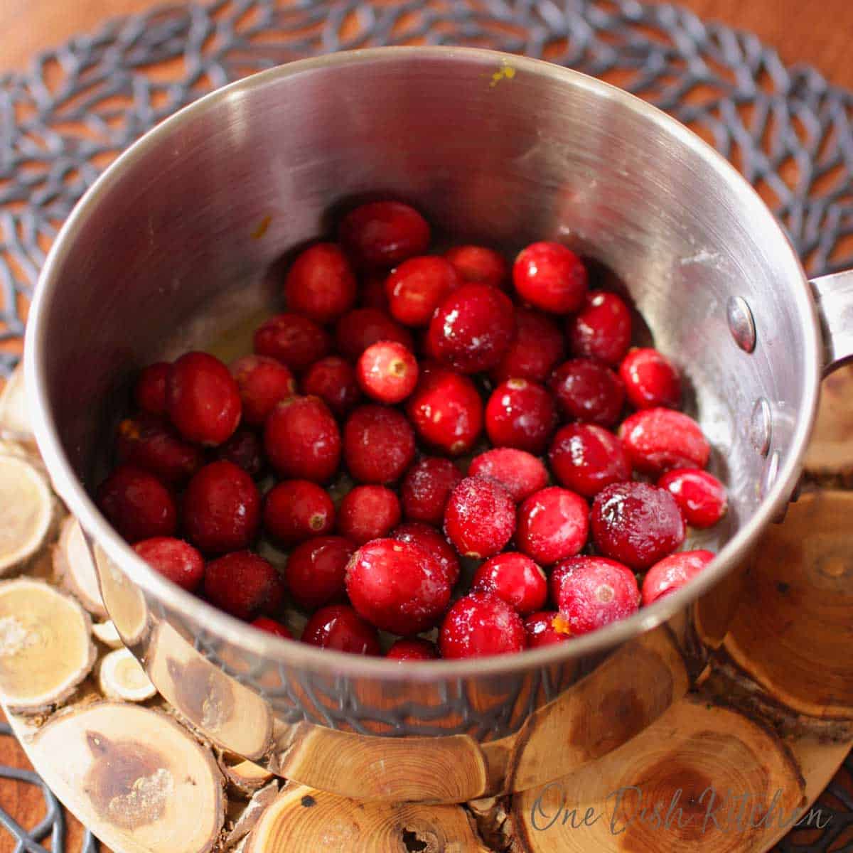 Cranberries and sugar in a pot on a wooden trivet.
