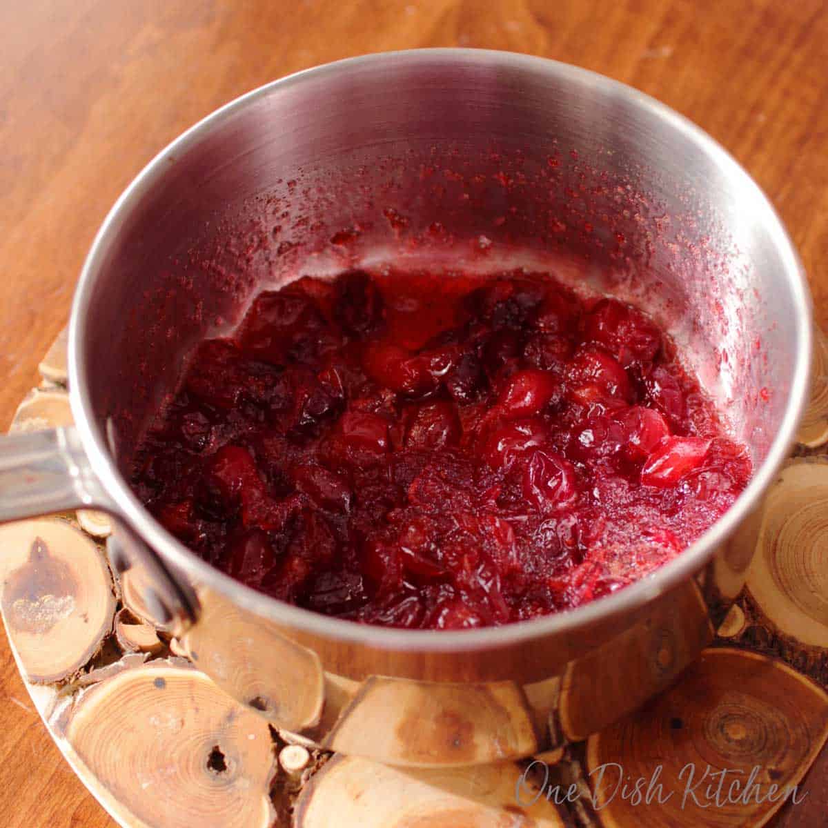 Cranberry jam in a pot on a wooden trivet.