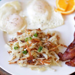 hash browns on a plate next to two strips of bacon and two over-easy eggs