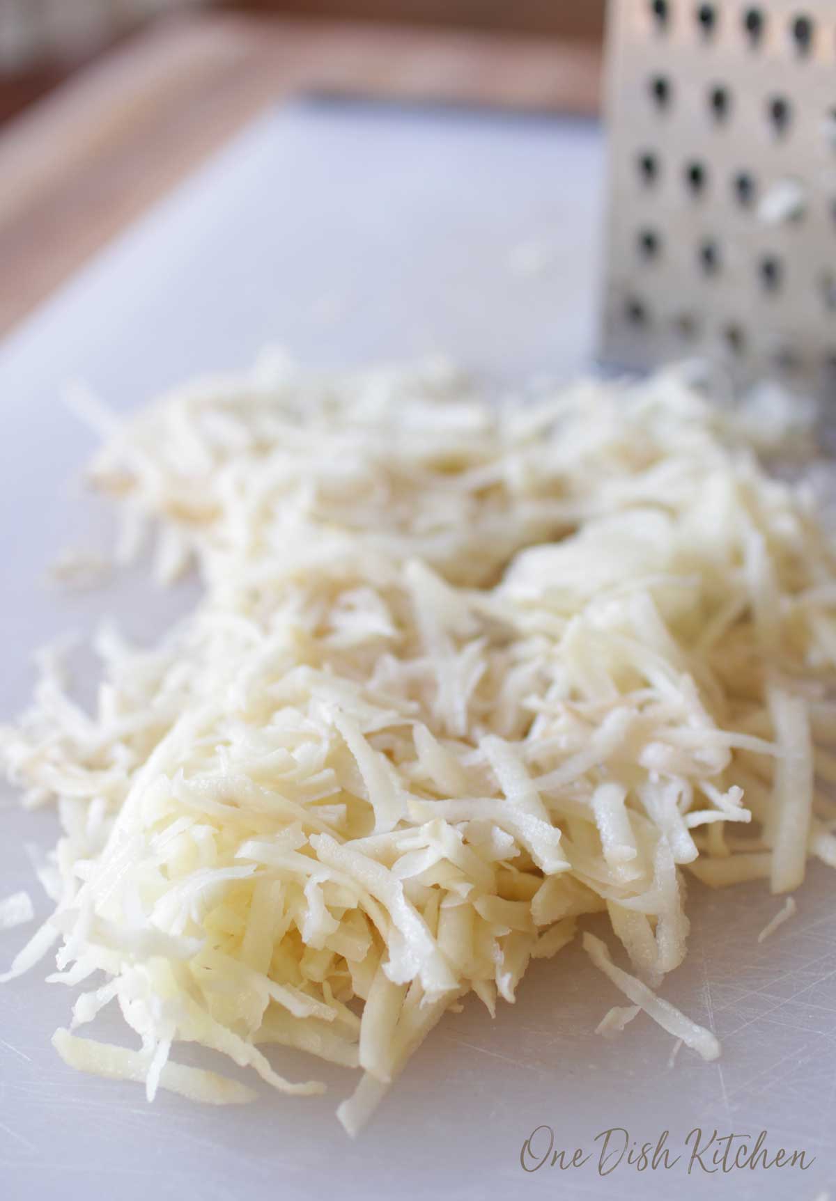 Shredded potatoes next to a cheese grater.