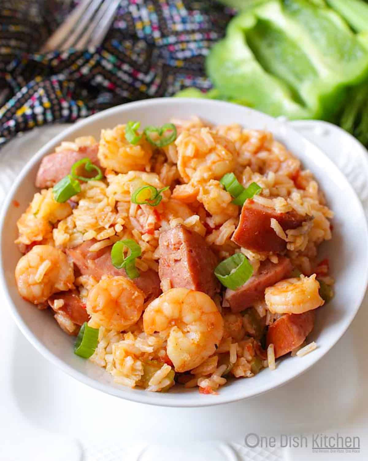 Shrimp and sausage jambalaya in a bowl with onions, celery, and green bell peppers in the background.