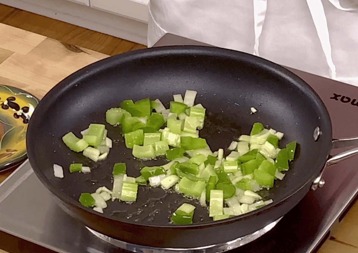 onions, bell peppers, and celery cooking in a skillet.