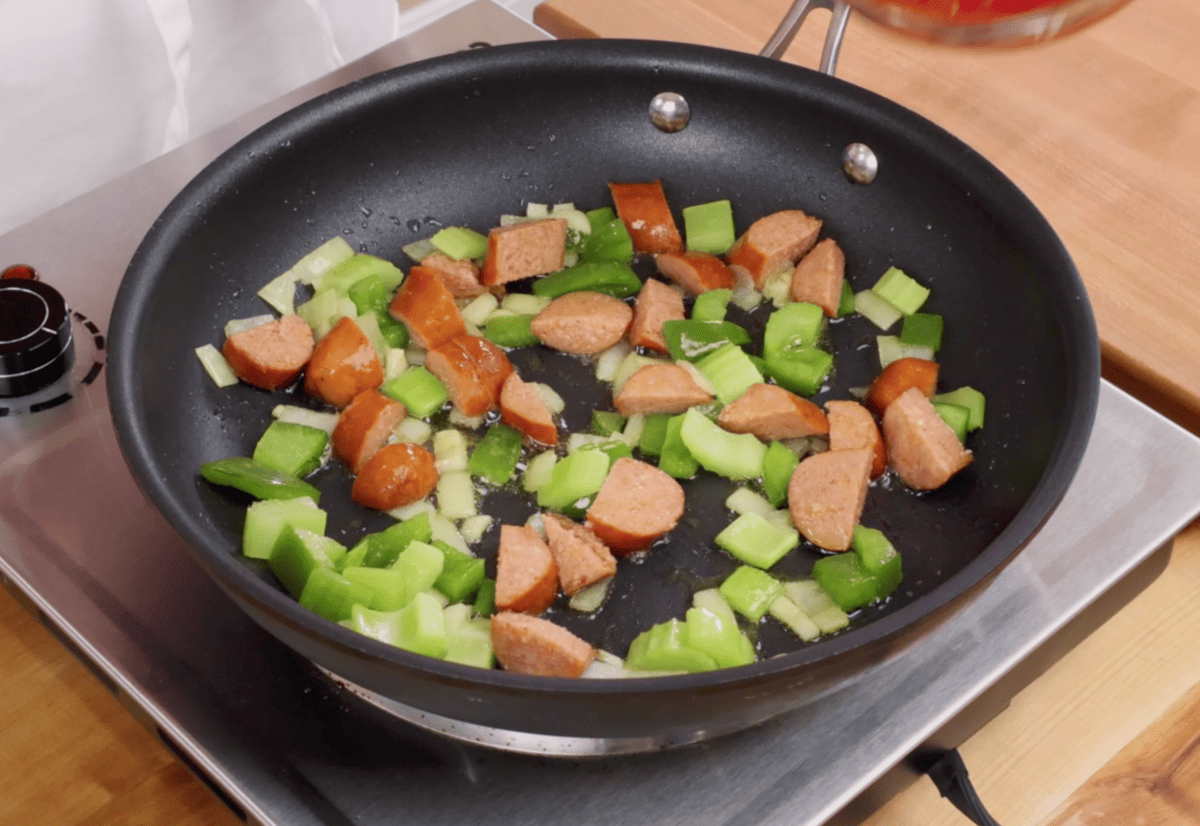 sausage, onions, and peppers cooking in a skillet.