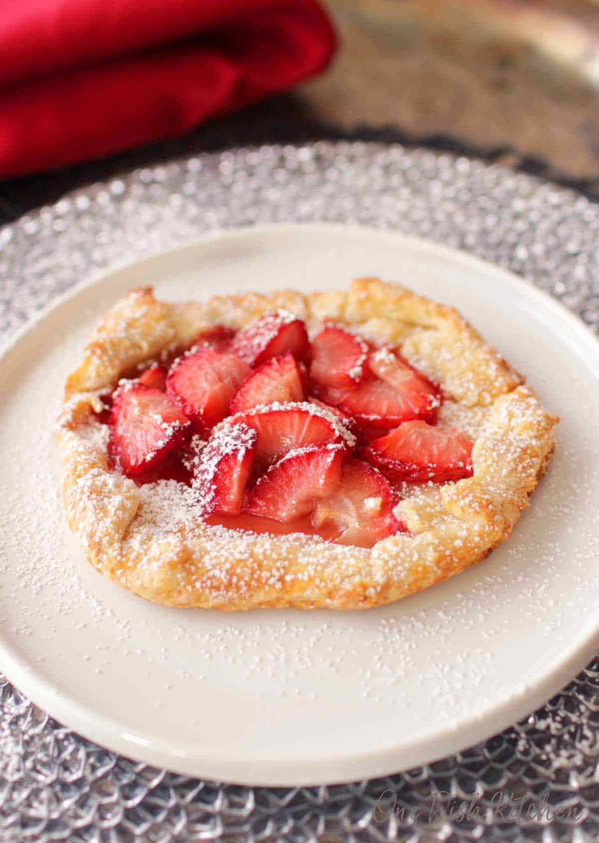 Pie crust with fresh sliced strawberries and dusted with powdered sugar on a plate.