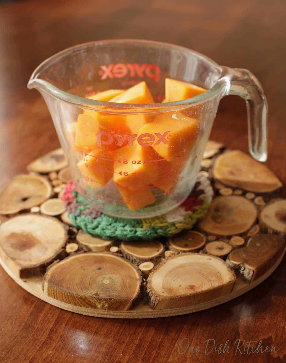 Cubed raw butternut squash in a measuring cup on a wooden trivet