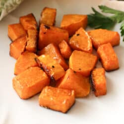 a plate of roasted butternut squash next to a sprig of parsley.