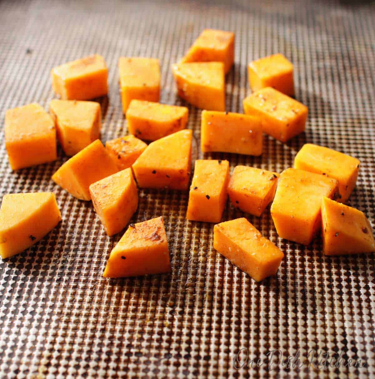 Cubed butternut squash seasoned on a baking sheet before roasting in the oven