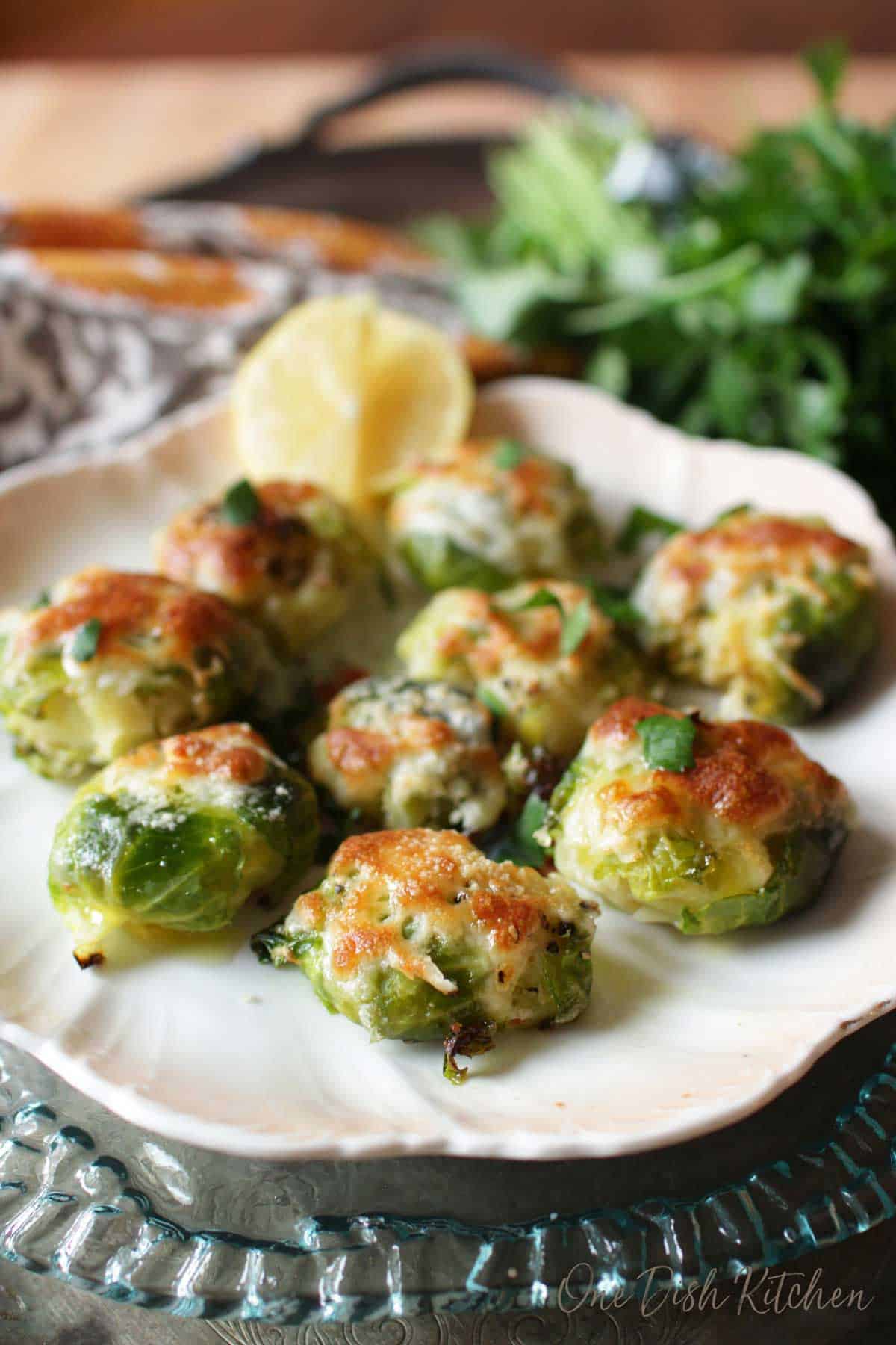 A plate of cheesy smashed brussels sprouts garnished with lemon slices.
