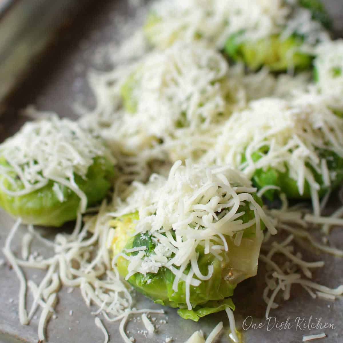 Shredded cheese on top of brussels sprouts on a baking sheet before roasting.