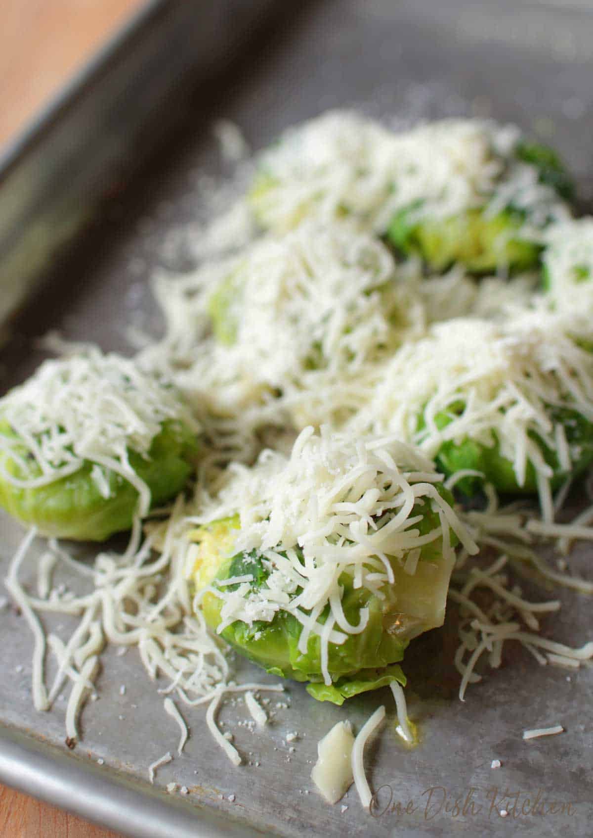 Shredded cheese on top of brussels sprouts on a baking sheet before roasting.