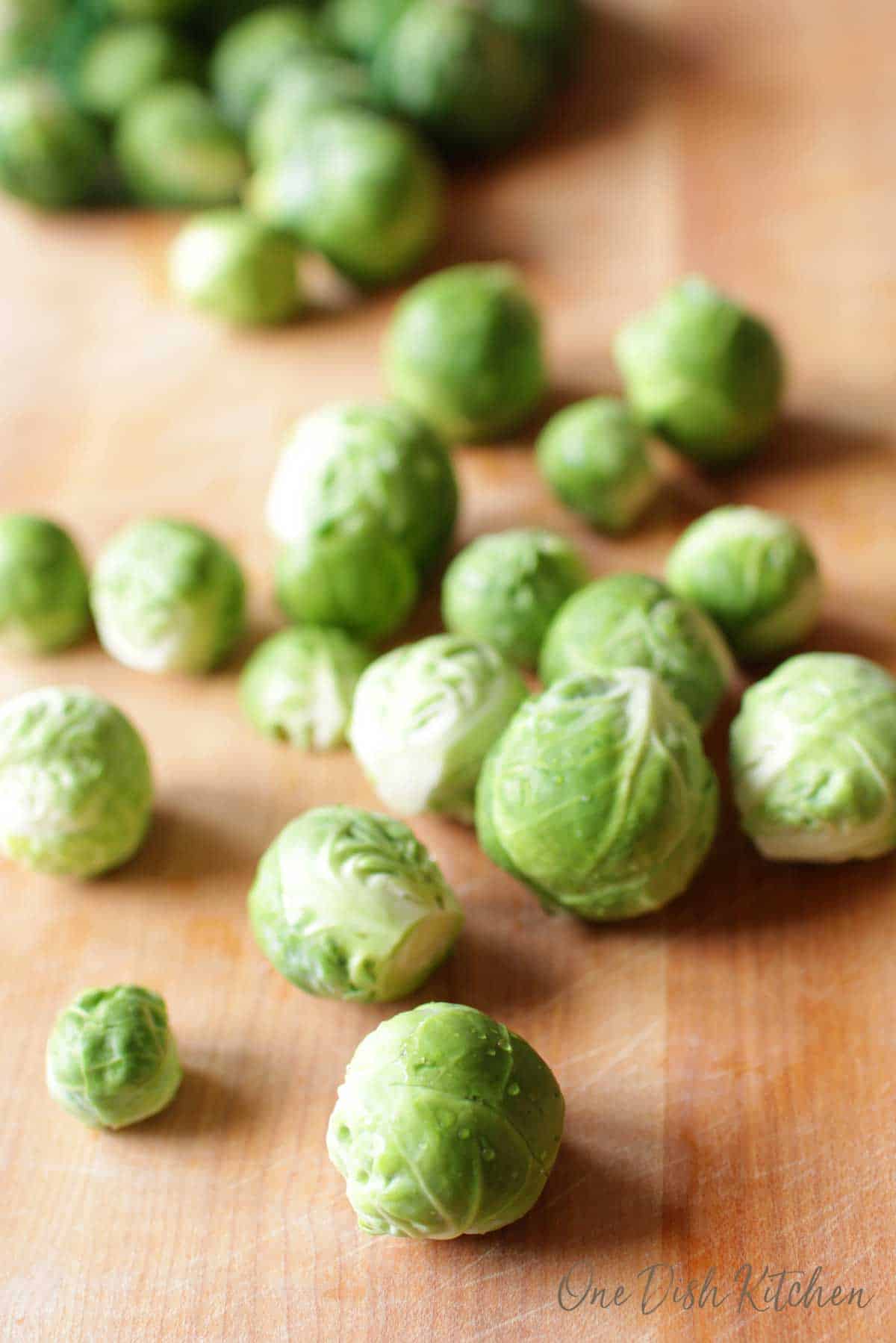 Raw brussels sprouts scattered on a wooden cutting board.