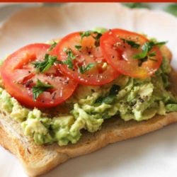 a slice of bread topped with mashed avocados and three slices of tomatoes