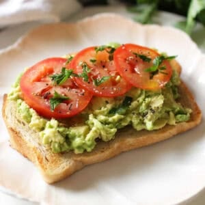 a slice of avocado toast topped with fresh avocado and slices of tomato.