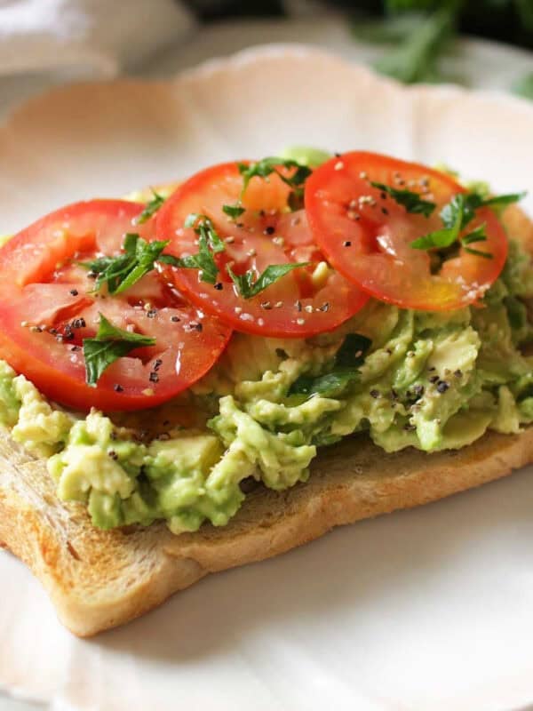 a slice of avocado toast topped with fresh avocado and slices of tomato.