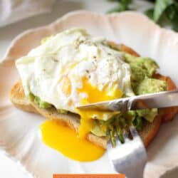 avocado toast topped with a fried egg on a white plate.
