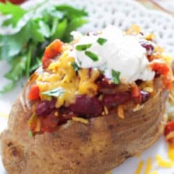 a chili cheese baked potato on a white plate.
