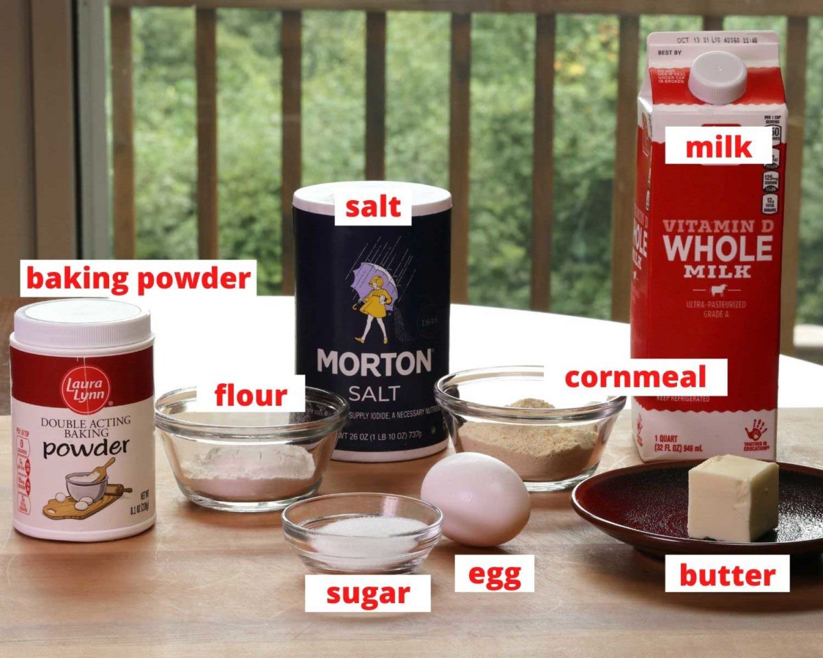 flour, cornmeal, salt, milk, egg and butter on a wooden cutting board.