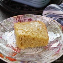a square piece of cornbread on a floral plate next to a pan filled with three squares of cornbread