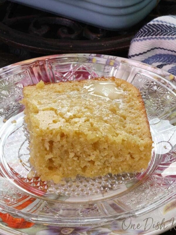 a square piece of cornbread on a floral plate next to a pan filled with three squares of cornbread