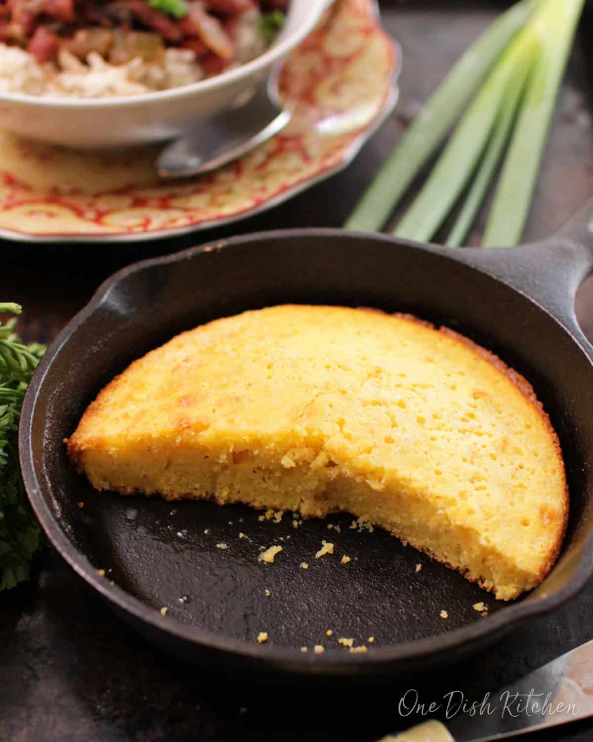 Cornbread cut in half in a small cast iron skillet next to a bowl of red beans and rice.
