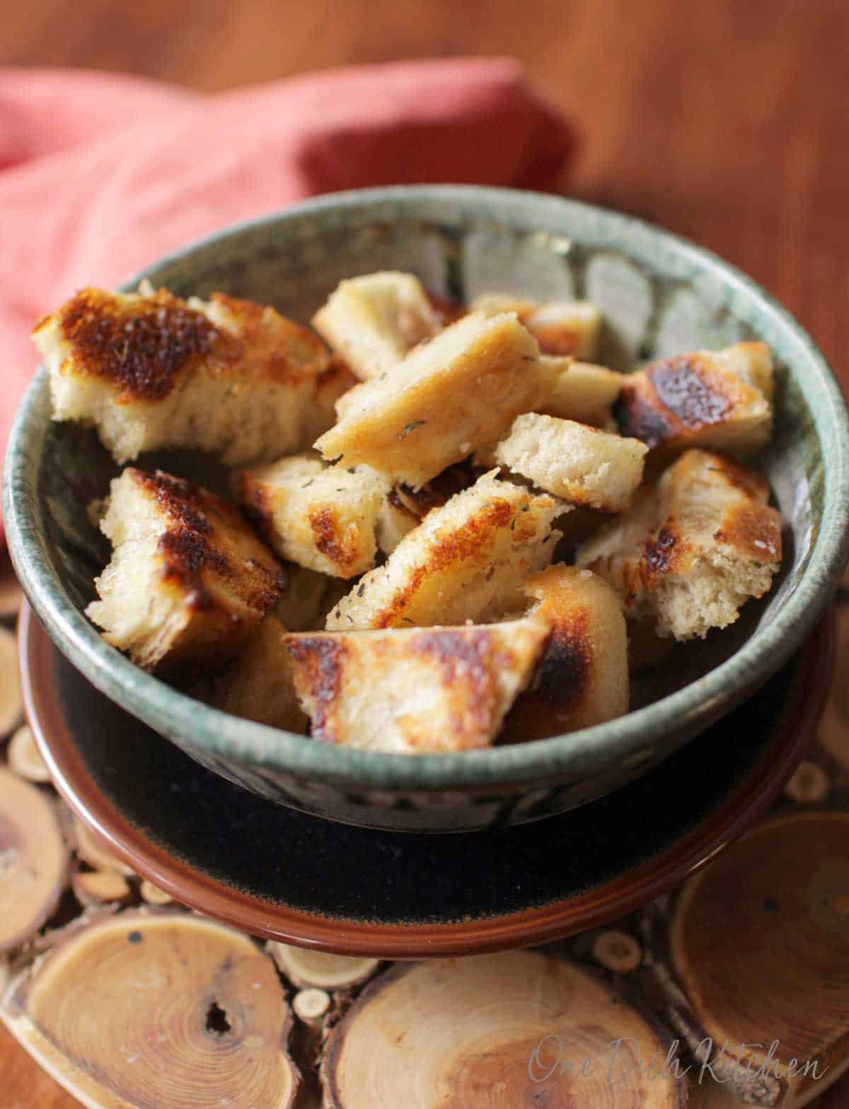 A closeup of a bowl of homemade croutons on a wooden trivet