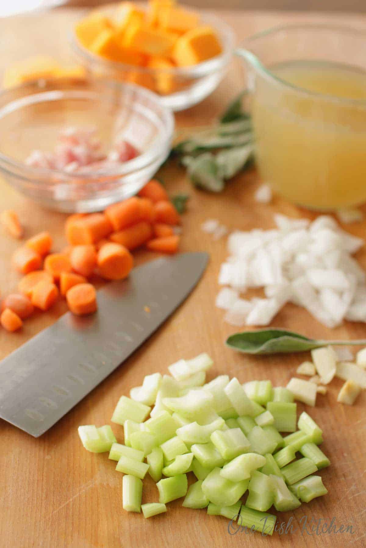 Ingredients needed in and Instant Pot Butternut Squash Soup- chopped celery, garlic, onions, carrots, butternut squash, chicken broth in a measuring cup, sage, all next to a large cutting knife.