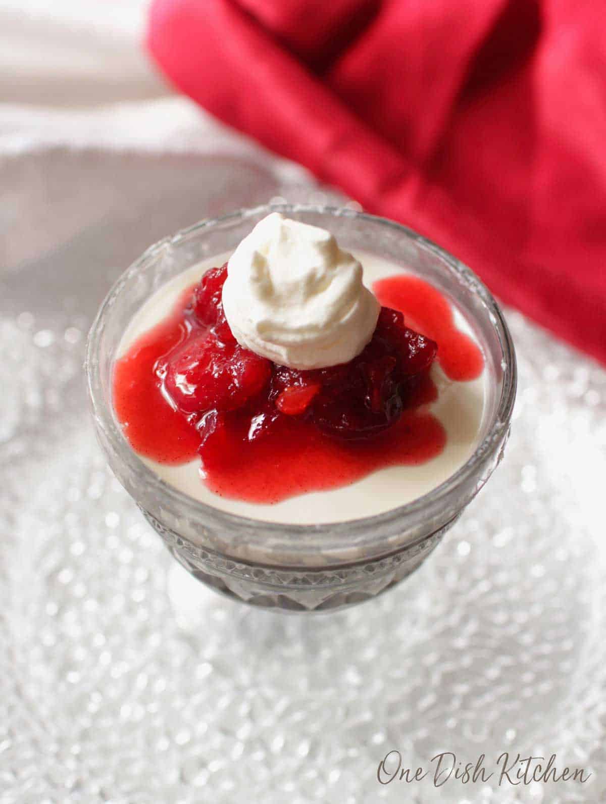 An overhead view of panna cotta topped with cranberry jam and whipped cream in a dessert glass