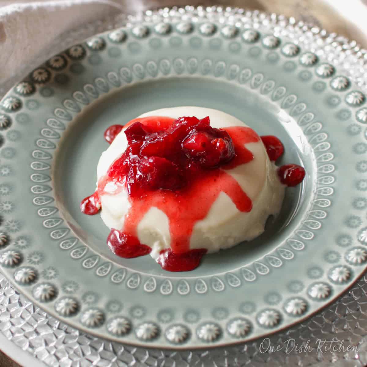 an unmolded panna cotta on a green plate topped with fruit sauce.