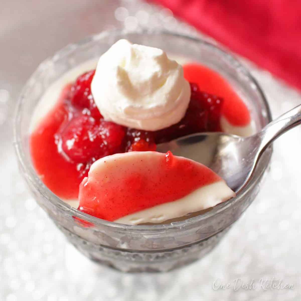 a small panna cotta topped with fruit sauce and a spoon on the side.