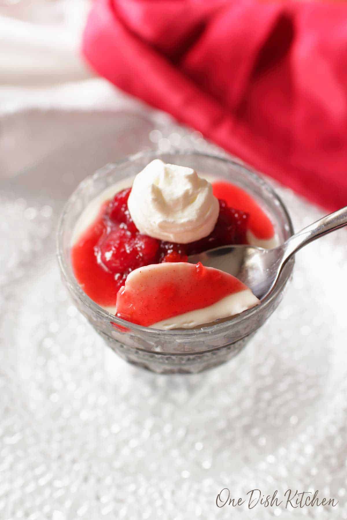 A spoonful of panna cotta topped with cranberry jam and whipped cream in a dessert glass