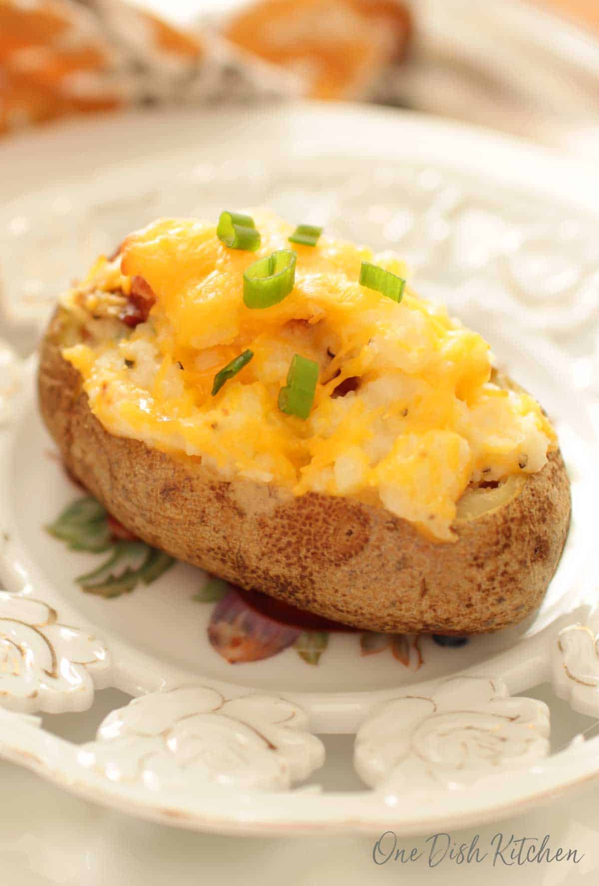 Twice baked potato on a plate topped with cheese and chopped green onions
