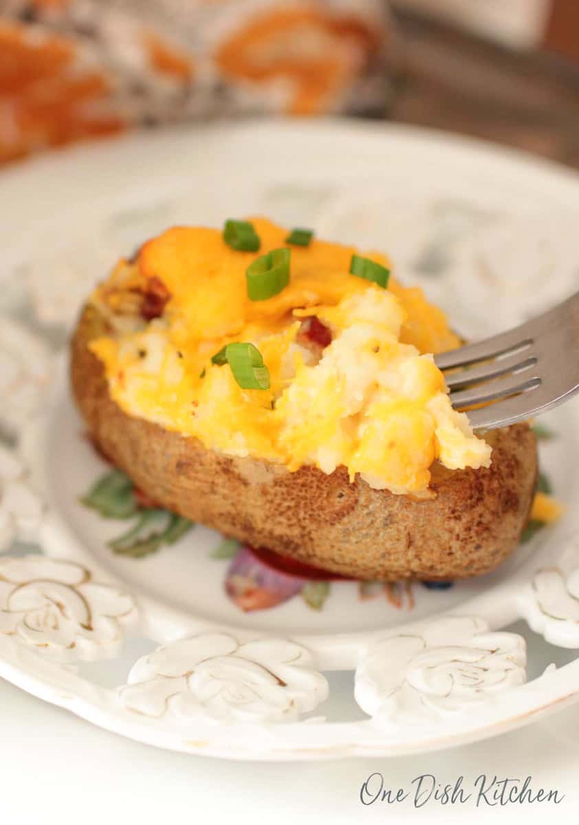 twice baked potato topped with sliced green onions and a fork on a plate.