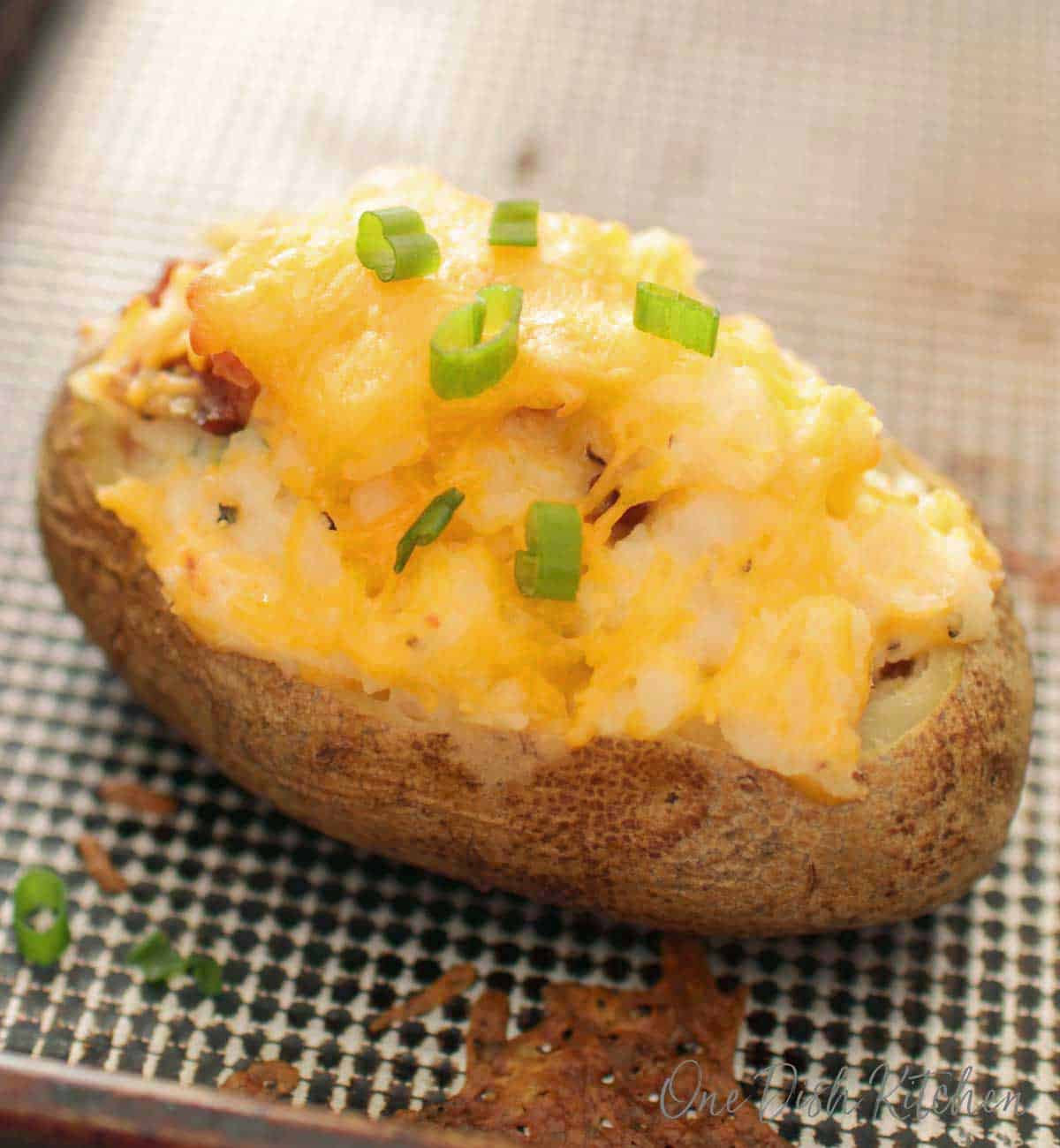 Twice baked potato on a baking sheet topped with cheese and chopped green onions