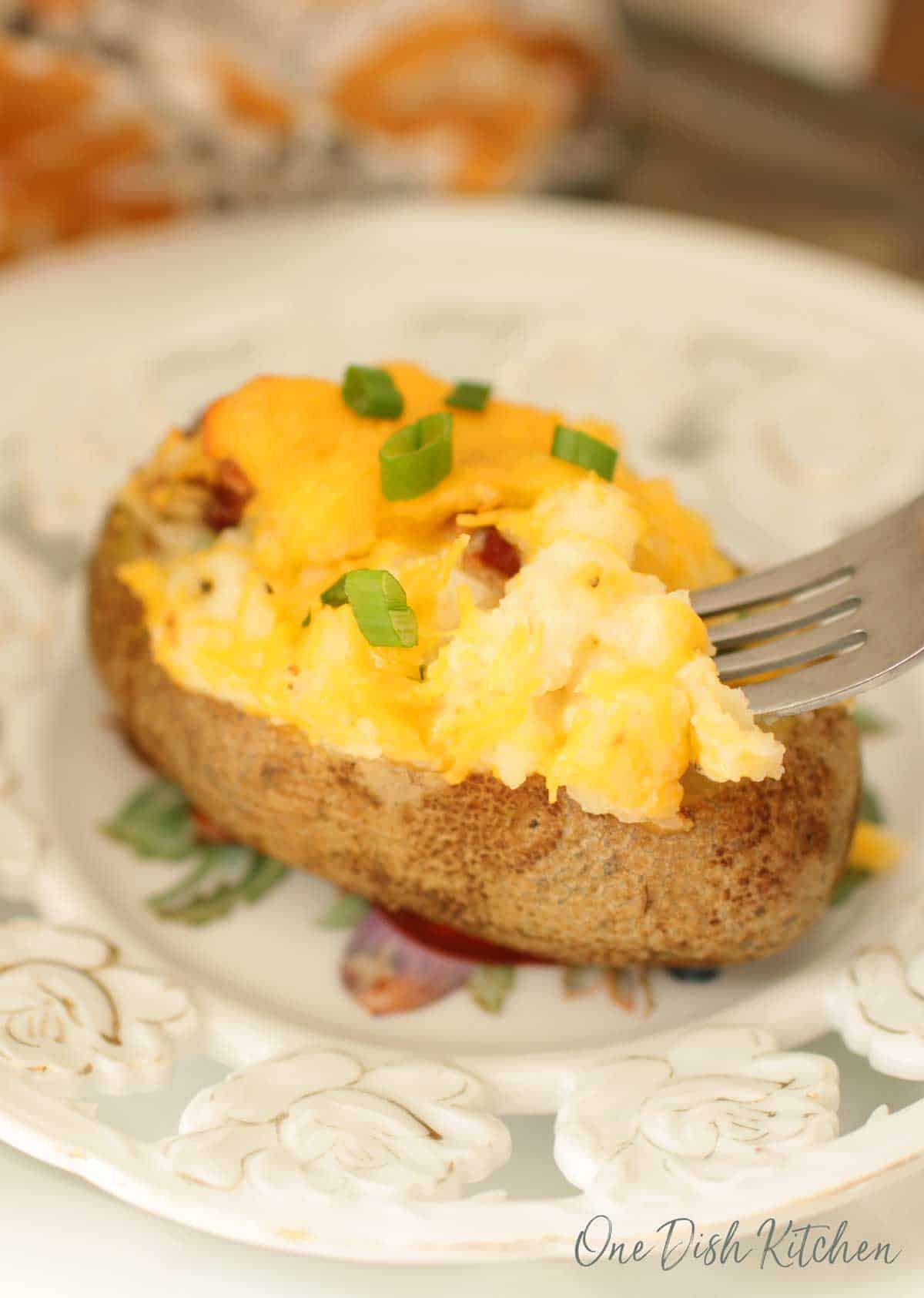 A fork diving into a twice baked potato on a plate topped with cheese and chopped green onions