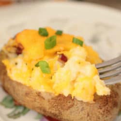 a baked potato on a white plate topped with green onions, bacon and cheese.