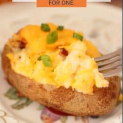 a cheese topped twice baked potato on a plate with a fork on the side.